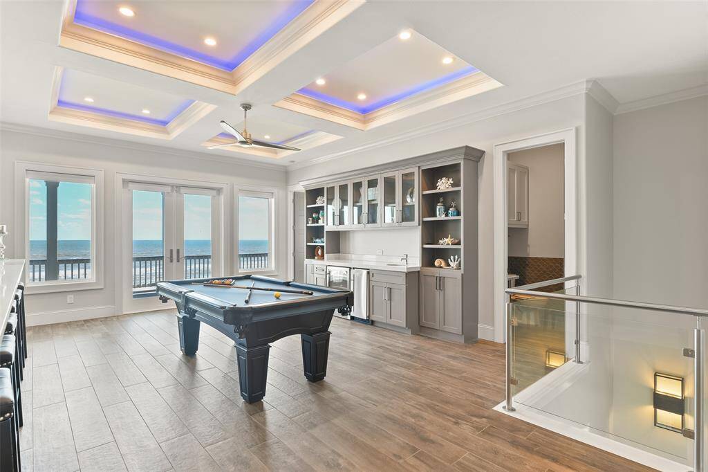 The upstairs game room offers a perfect retreat, complete with elegant tray ceilings, custom LED lighting, a pool table, and a custom wet bar with built in shelves, cabinetry and an ice maker. It's the ideal space for entertaining and relaxation.