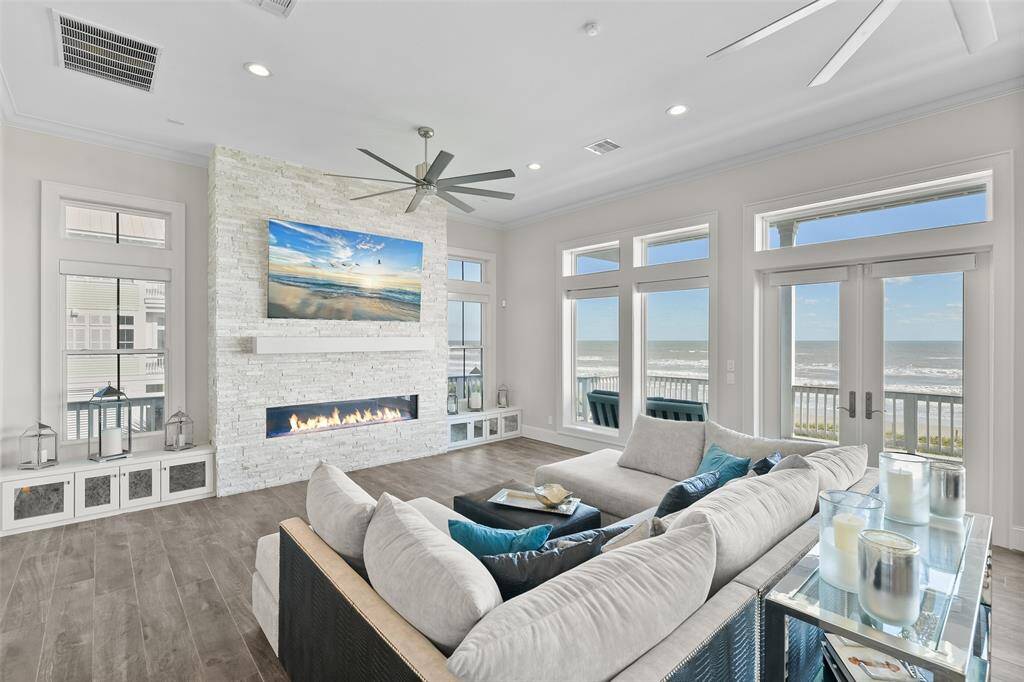 Relax in style in this custom-furnished and sophisticated living room featuring an 80" brand new TV, a modern 72" rectangular direct vent fireplace, custom built-ins, luxury tinted windows, and storm doors. Designed for comfort and elegance, this space offers the perfect blend of warmth and coastal charm with stunning views just beyond.