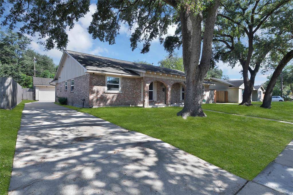 This South-facing single-story brick home featuring a well-manicured lawn, mature shade trees to the South, detached garage at the end of a single driveway.