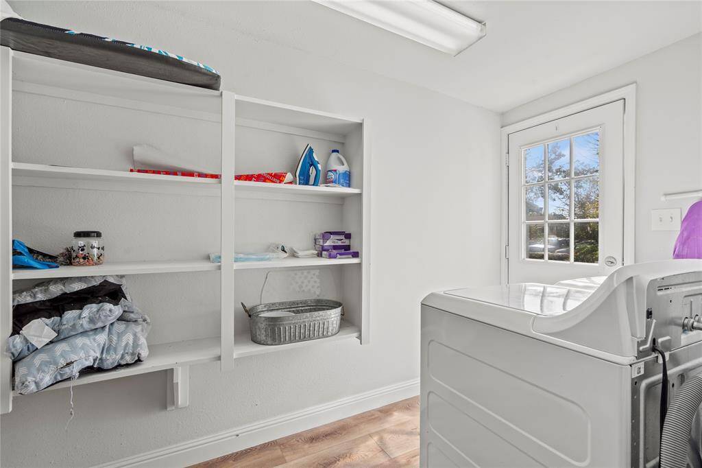 Enjoy the convenience of a generous laundry room adjacent to the kitchen, complete with ample shelving and modern white appliances included with the purchase.
