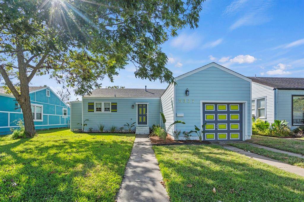 Charming single-story home with a light blue exterior and vibrant yellow door, featuring a neat front lawn with a mature tree, and a welcoming walkway leading to the entrance.