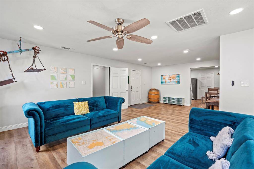 This is a modern, open-plan living space featuring bright, airy interiors with recessed lighting, a vibrant blue sofa set, a sleek dining area in the background, and contemporary decor elements. It appears well-maintained and move-in ready.