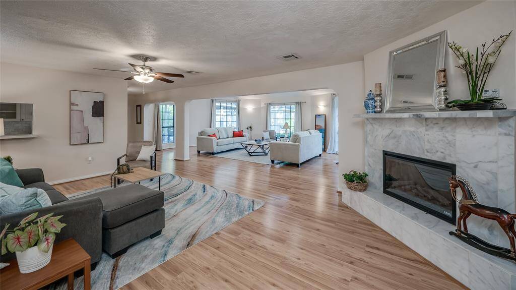 This is a spacious and well-lit den featuring light laminate flooring, a modern fireplace with a marble surround, and an open layout that flows into an adjoining room. The neutral color palette and contemporary furnishings create a welcoming atmosphere.