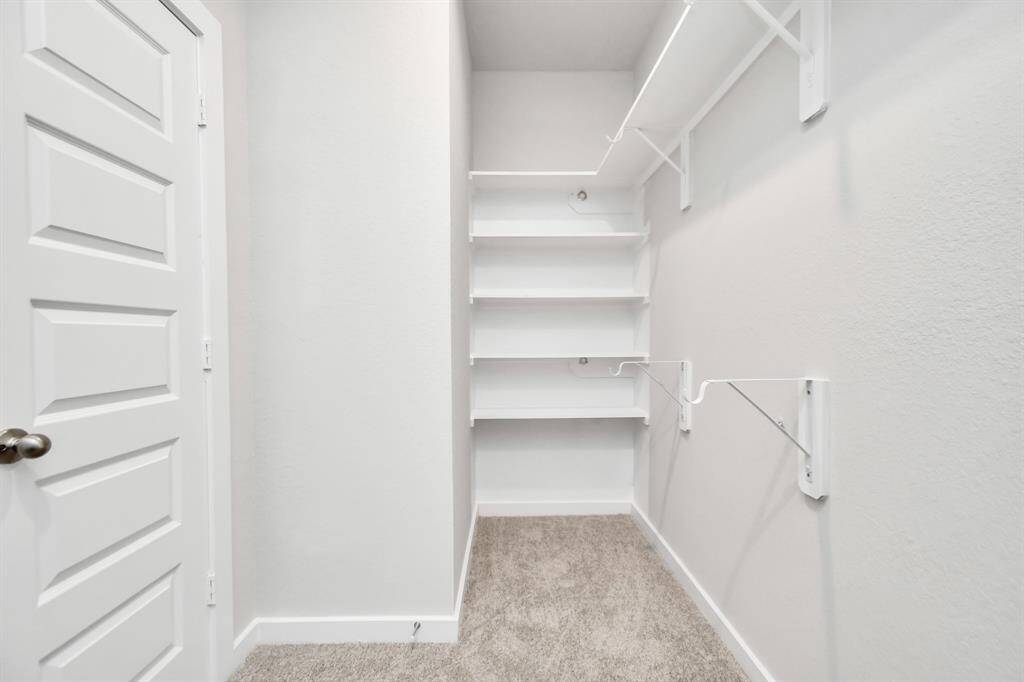 Experience luxury in this spacious walk-in closet with high ceilings and plush carpet. Warm paint tones, built-in shelving, and dark finishes create a contemporary and functional retreat