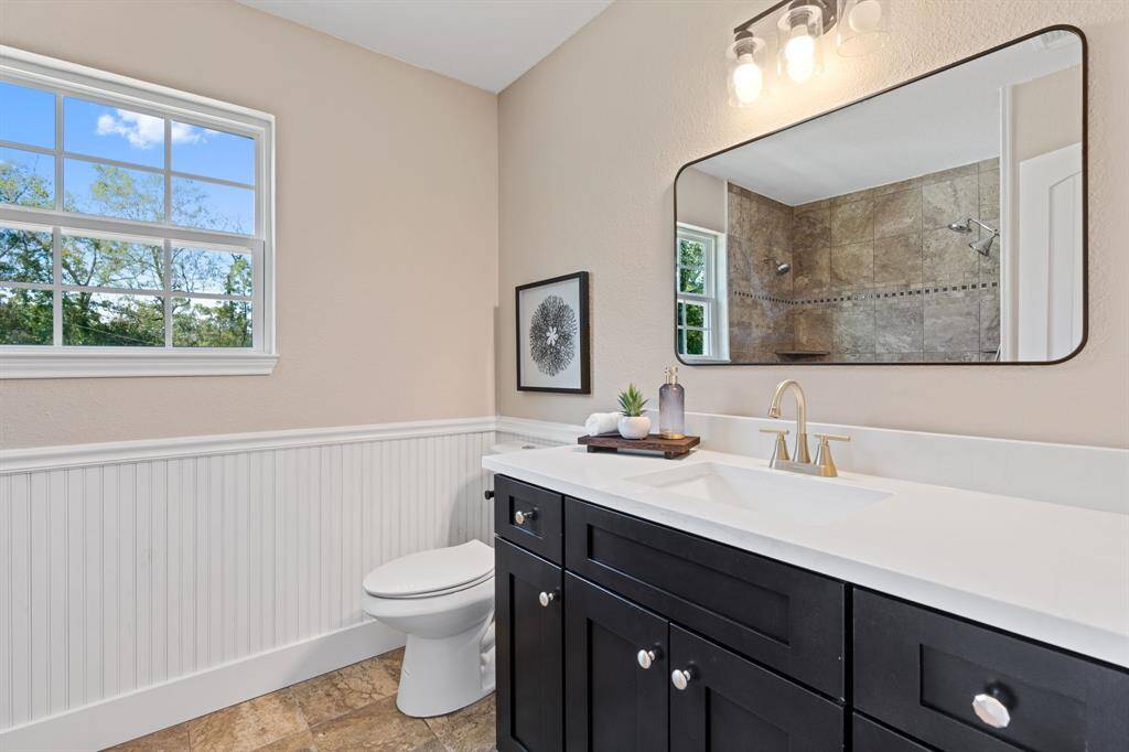 The primary bathroom features dark cabinets, white counters, tile floors, and a large window.