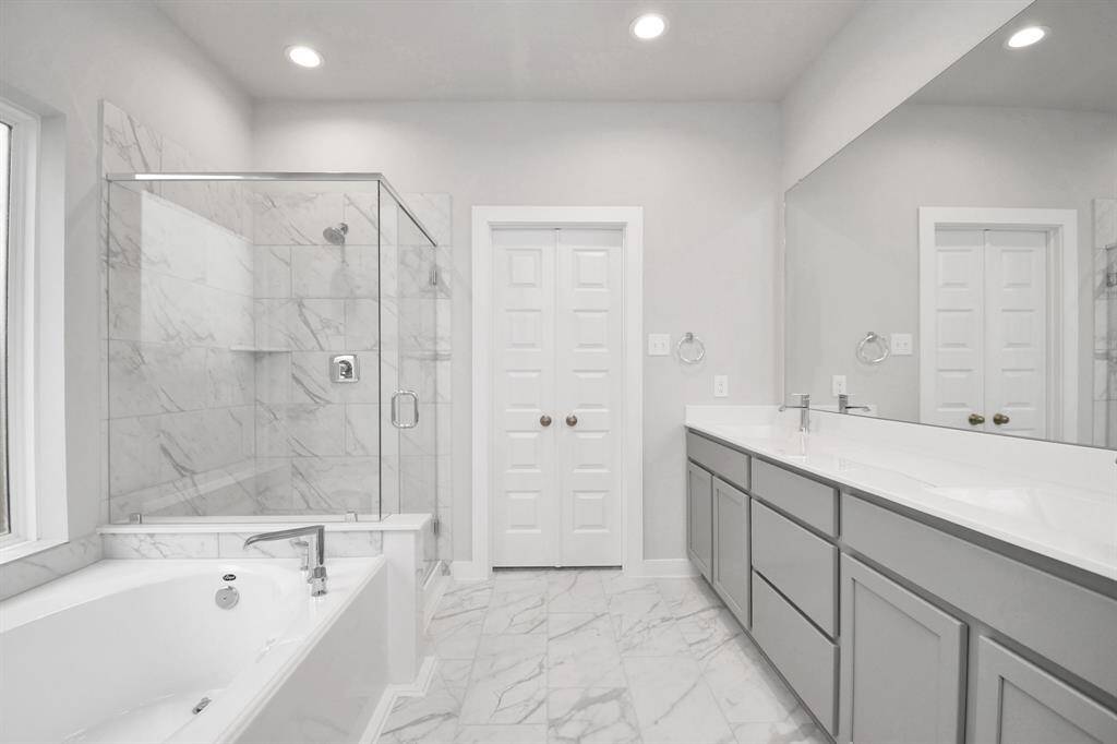 The expansive walk-in shower, surrounded by tile, and the distinctive garden tub with unique accents elevate your daily routine. The sophisticated vanity, featuring double sinks, light-colored countertops, contemporary hardware, and bright recessed lighting, adds both style and functionality to the space.