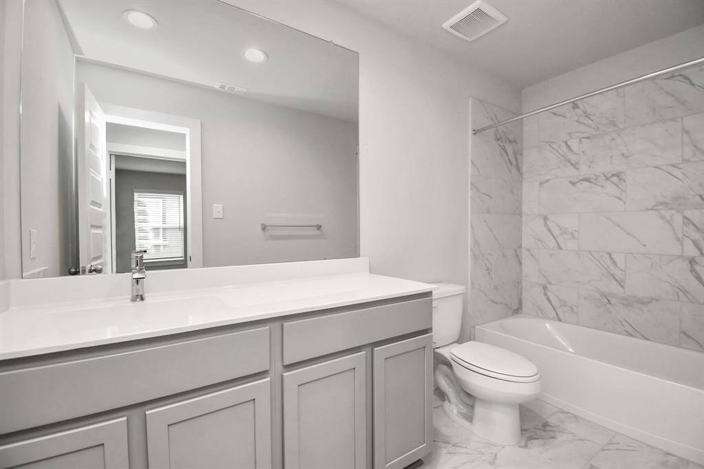 The secondary bath boasts stylish tile flooring, a bath/shower combo with a sleek tile surround, light wood cabinets, and a stunning light countertop.