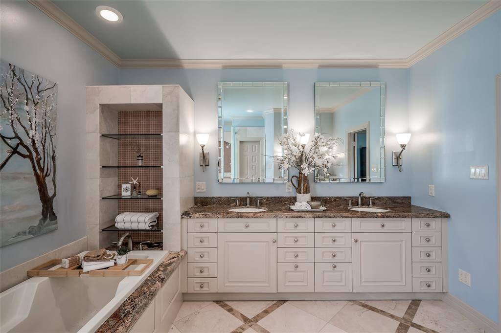 Sophisticated bathroom featuring a soaking tub, dual sinks, elegant built-in shelving, and sconce-lit mirrors.