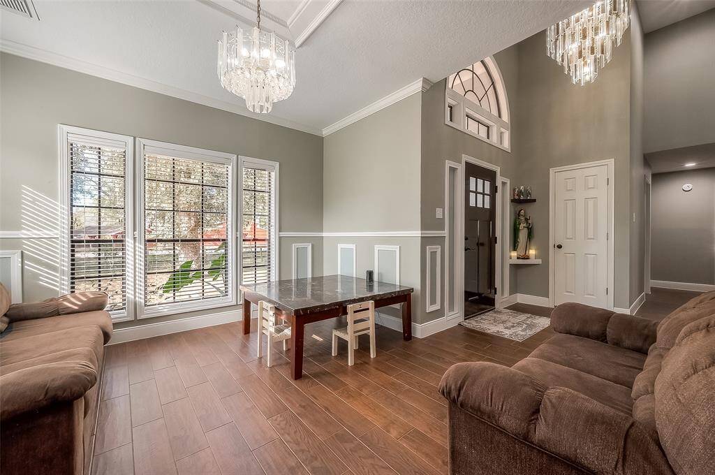 The photo showcases a spacious and well-lit formal dining over looking the entry with elegant chandeliers and large windows that offer plenty of natural light.