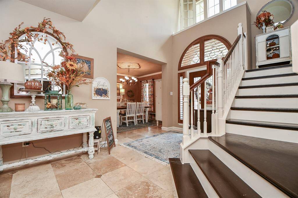 This exquisite view of the front entry from the inside is magical; with a beautiful view of the wood tread staircase; high ceiling with windows up and down, travertine flooring and an open view of your formal dining space, up center.