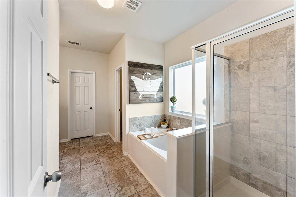 Bright And Modern Bathroom Featuring A Large Soak Tub, A Glass-enclosed Shower With Tile Surround, And A Window Providing Natural Light. The Space Is Finished With Tiled Flooring.
