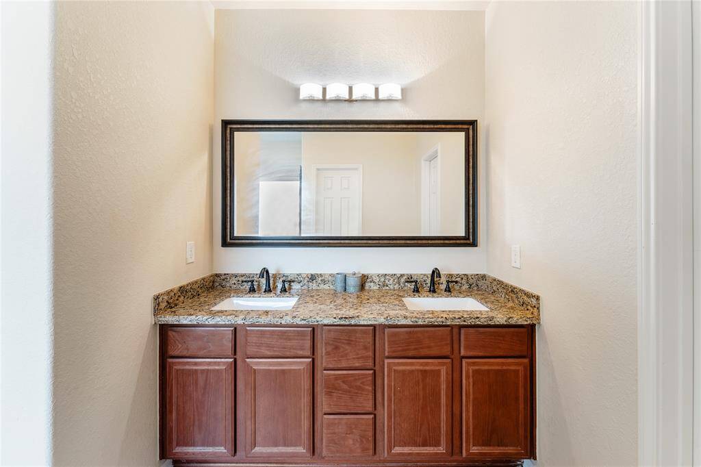 This is a neat, bathroom vanity featuring a granite countertop, undermount sink, rich wooden cabinetry, and a large mirror with overhead lighting.