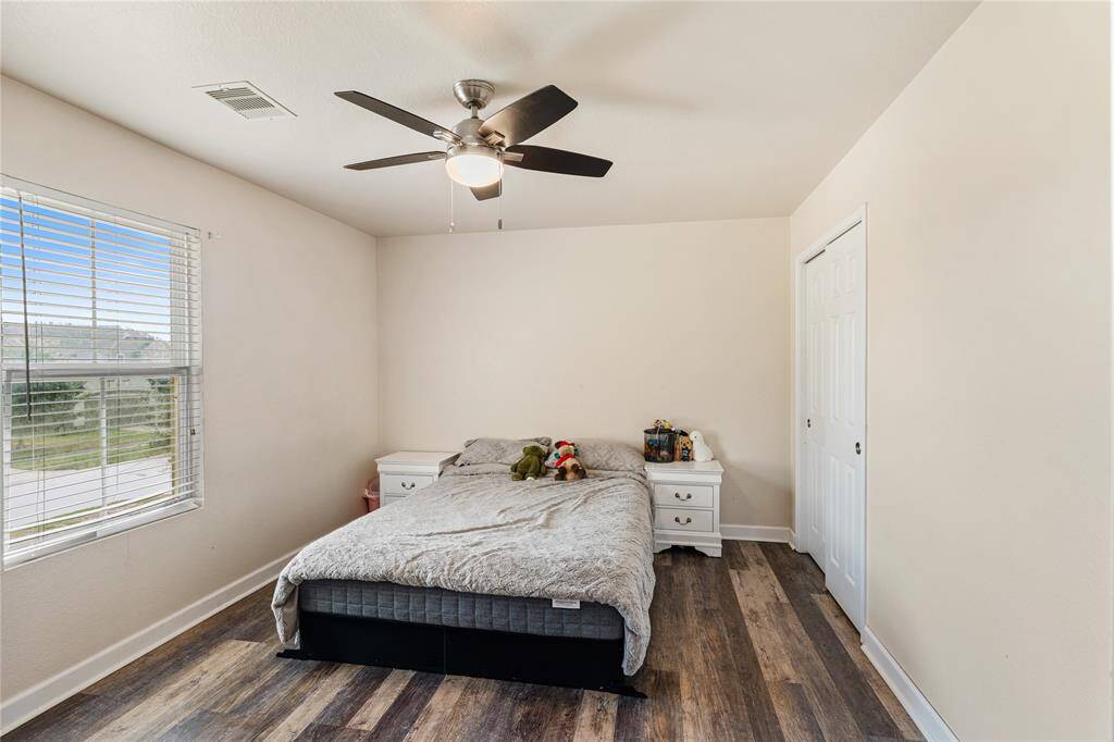 Bright and cozy bedroom featuring a ceiling fan with light, a large window for natural light, and modern wood-look flooring.