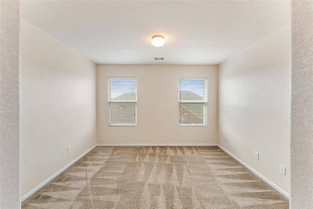 The room features neutral walls and carpeted flooring, with natural light coming in from two windows. It appears to be a clean, blank canvas for a potential home buyer.