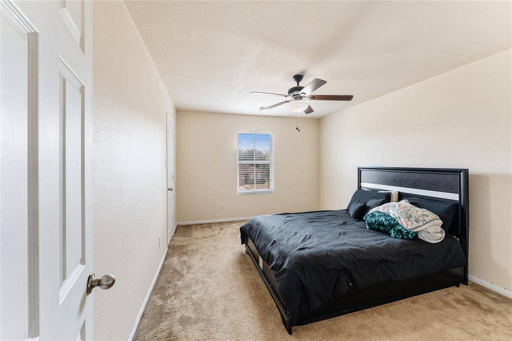 This is a well-lit, modest-sized bedroom featuring a ceiling fan, neutral wall colors, and carpeted flooring.