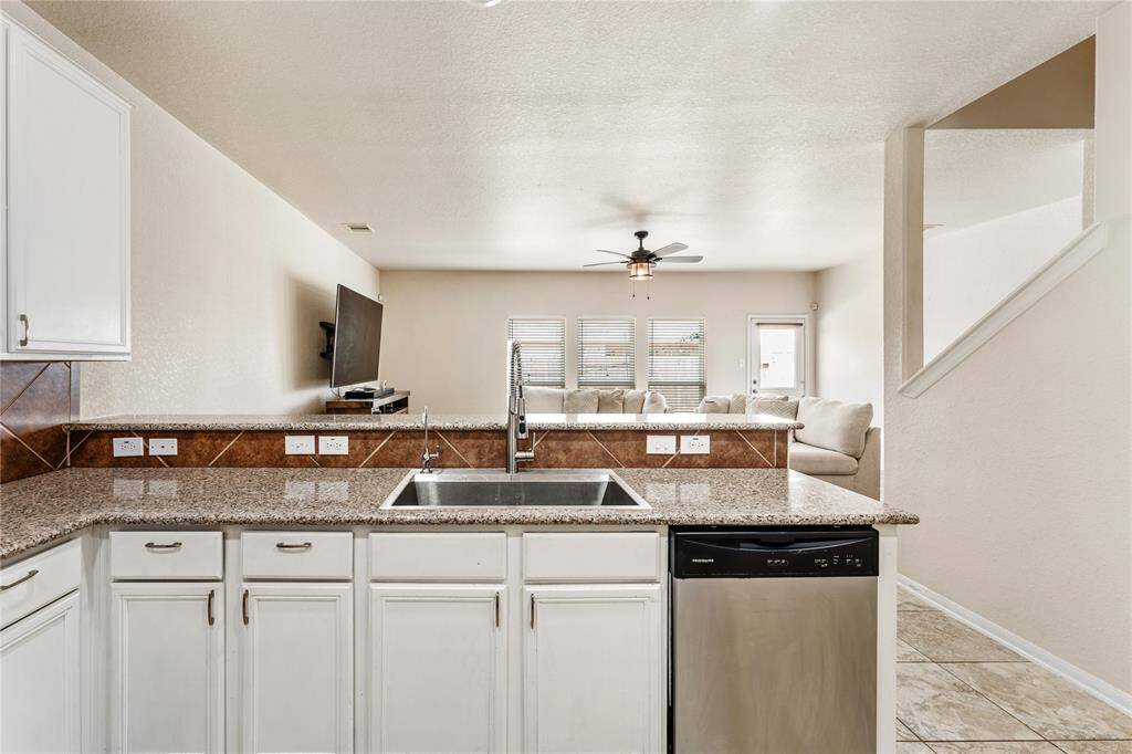 The Kitchen Features Modern Stainless Steel Appliances, White Cabinetry, Granite Countertops, And a Tile Backsplash. It Yields An Amazing View Of The Living Room and Back Yard
