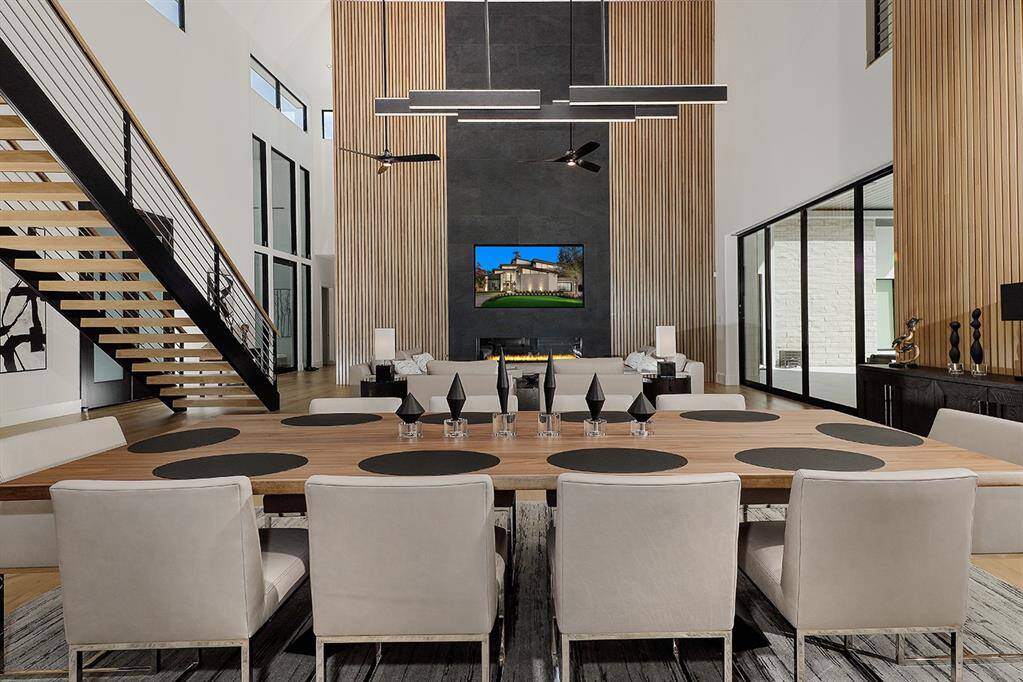 This is an open-concept living space with high ceilings and a striking staircase . It features a large open dining area  and a contemporary fireplace, complemented by wood accent walls and abundant natural light from floor-to-ceiling windows.