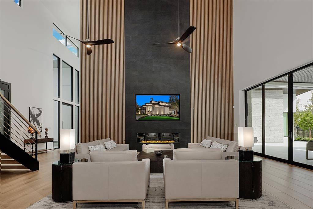 Open living room with large windows, and a cozy fireplace and slatted wood accent walls. All windows throughout have Lutron shades sheer and blackout.