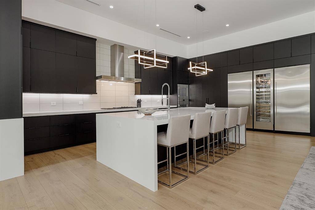 Modern kitchen with sleek black cabinetry, white quartz countertops, a large island with bar seating and stylish pendant lighting. All interior cabinets are clear birchwood w/soft close drawers and doors.