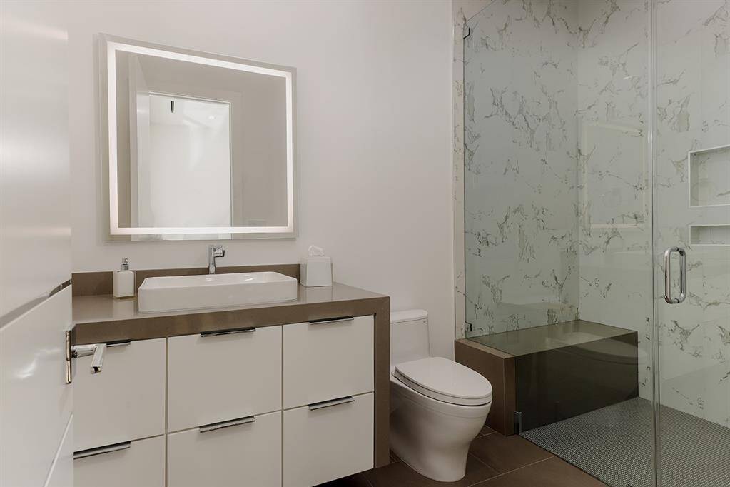 4th bathroom with sleek finishes, featuring waterfall quartz vanity with a vessel sink and lighted mirror.