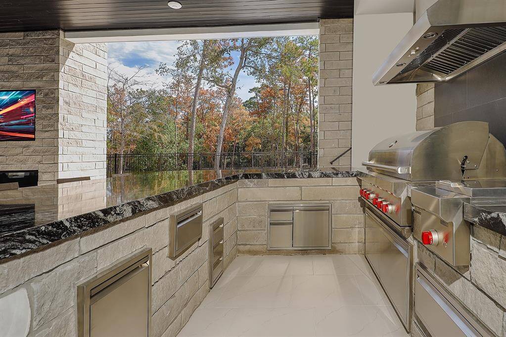 Covered outdoor kitchen featuring stainless steel  Wolf 54" stainless steel grill & side burner with 60" vent hood. Granite waterfall slab countertops. The space is well-lit and provides a beautiful view of the pool/spa and Lake Woodlands.