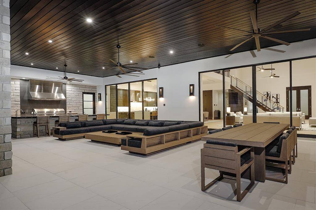 This is a spacious, modern open veranda  with a staircase leading to the upper level. The area is well-lit, with a warm wooden ceiling and multiple fans, and has a clean, contemporary design aesthetic.