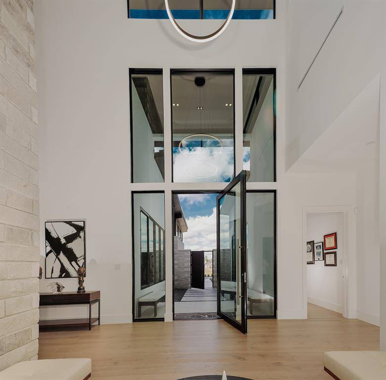This is a gated entryway featuring high ceilings, a 10' steel glass door, and a bright, open-concept design with clean lines. The space is accented by stone walls and sophisticated lighting fixture, with natural light enhancing the airy ambiance.