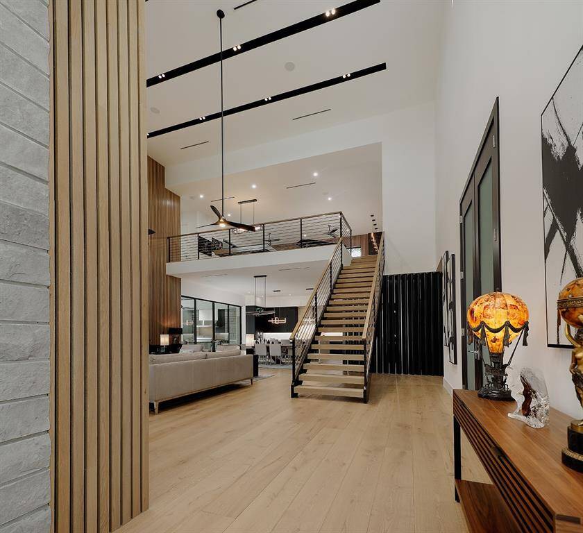 Show casing recessed lighting, an open-plan living area, a sleek staircase leading to the second with a balcony railing, hardwood floors, and a clean, contemporary design aesthetic. All 10' white oak plank engineered hardwood flooring.