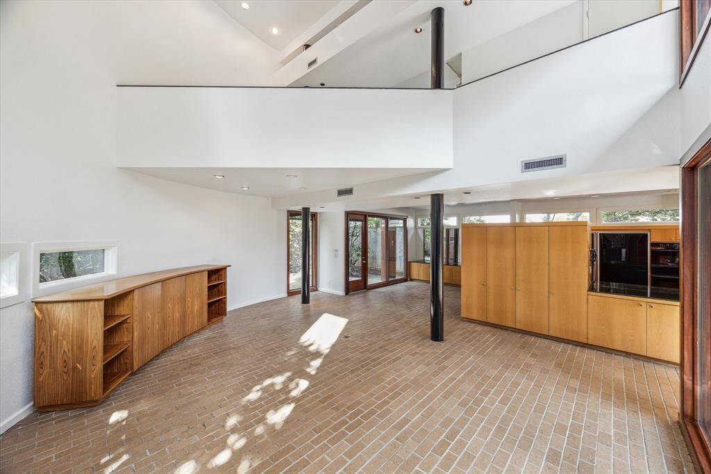 The living room of the home is at the end of the hallway. The open wall above is the primary bedoom.  The dining room is in the background with views of the back patio.  THere are numerous built-in cabinets throughout the home,