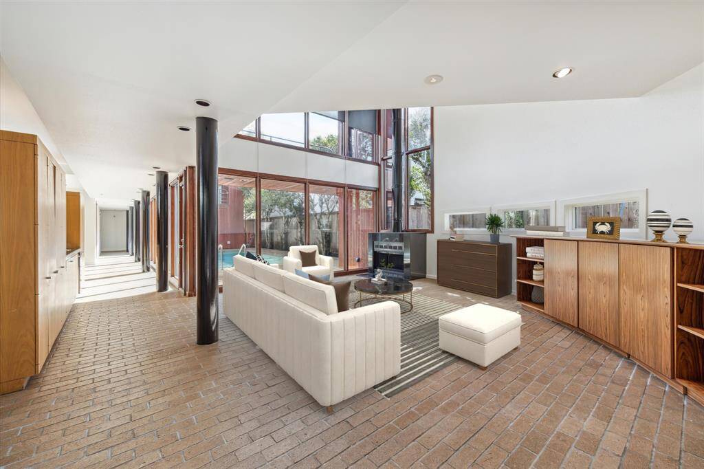 Virtually staged large living room with a free standing wood burjing fireplace, Two-story windows with pool and sky views. Virtually stages.