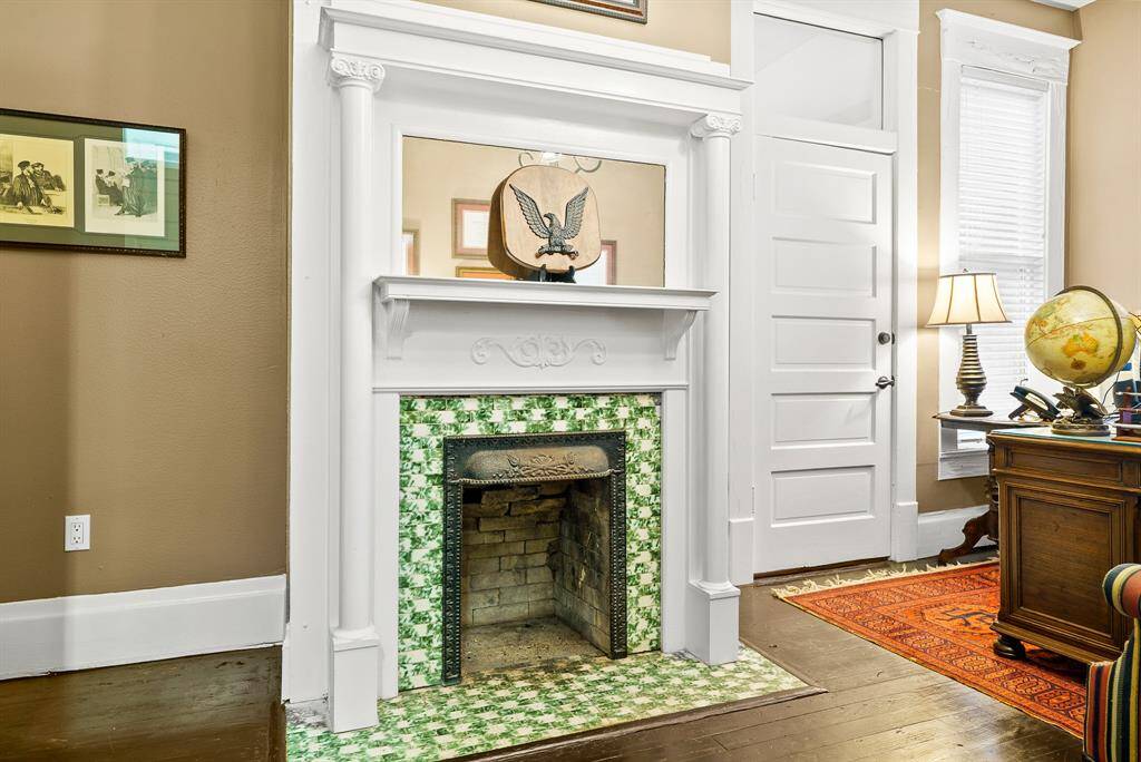 This antique, dual-sided fireplace boasts an ornate tile surround, wrought iron frame, and custom wood mantle with mirror inlay. The cased doorway to the right, with transom above, leads directly into the previously seen Conference Room.