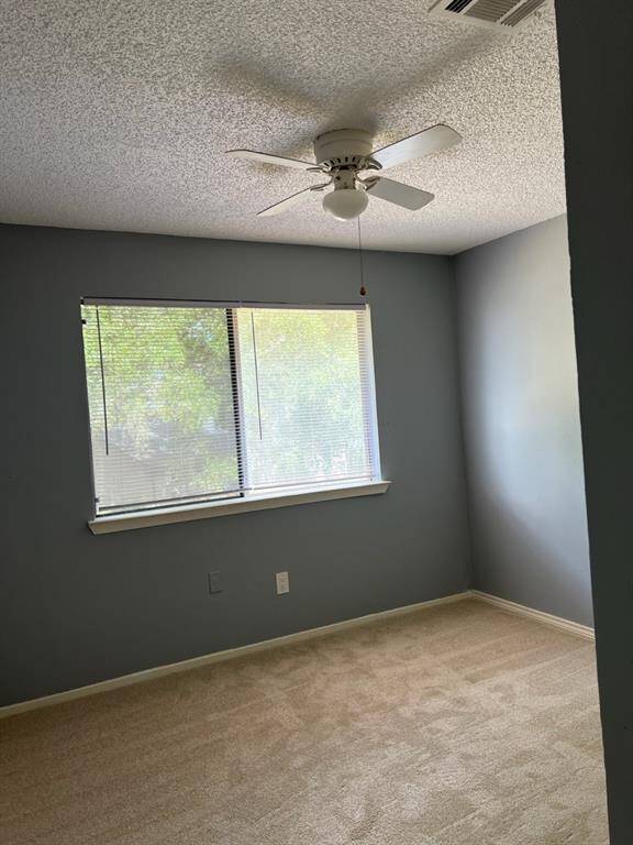 This is a well-lit, empty room featuring a neutral color scheme with a large window, carpeted flooring, and a ceiling fan.