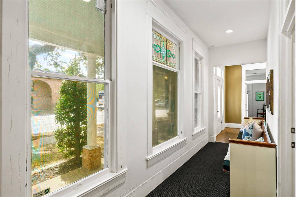 Here is another look at the hallway that connects one side of the building to the other. Three large windows usher in the natural light while also offering a panoramic view of the expansive Front Porch ahead. An ornate, stained-glass window adds a welcome pop of color.