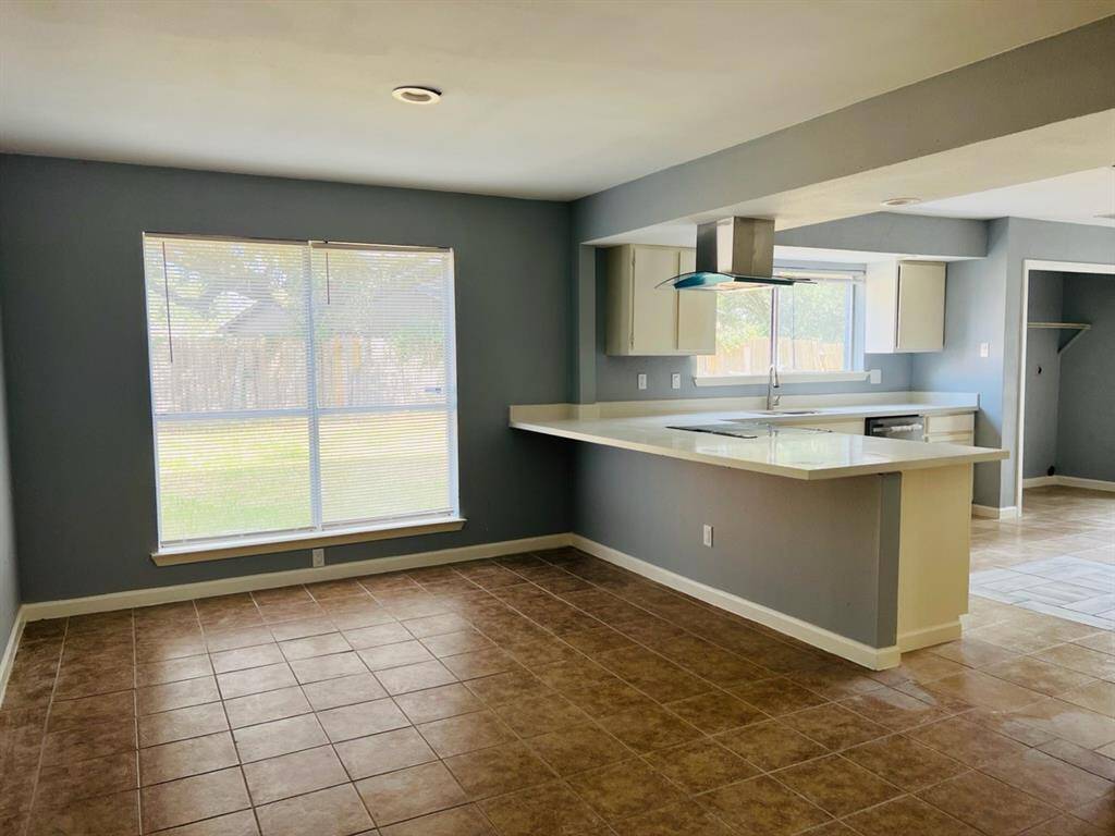 This image features a spacious, open-concept living area with a modern kitchen, large windows providing natural light, and tiled flooring, offering a clean and contemporary living space.