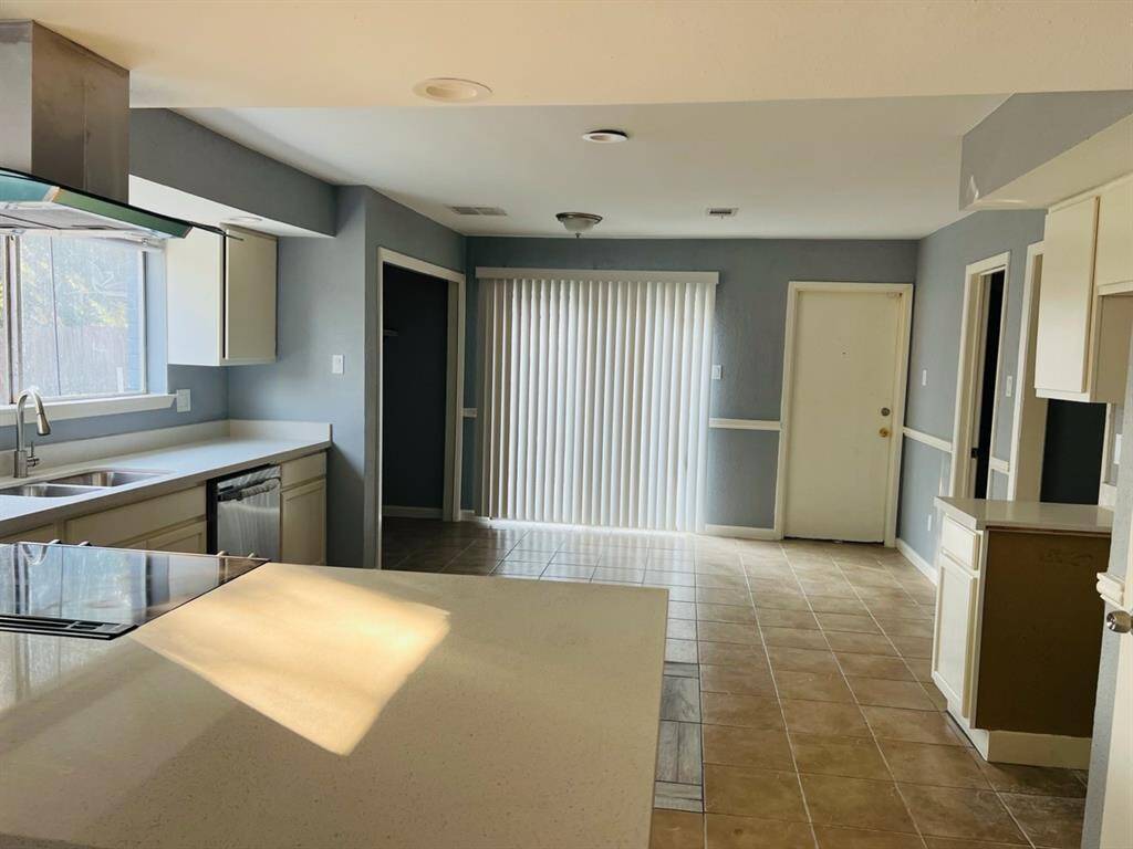 This is a spacious kitchen with modern appliances, ample counter space, and plenty of natural light. It features a tile floor, light-colored cabinetry, and a view into an adjacent room with sliding glass doors.