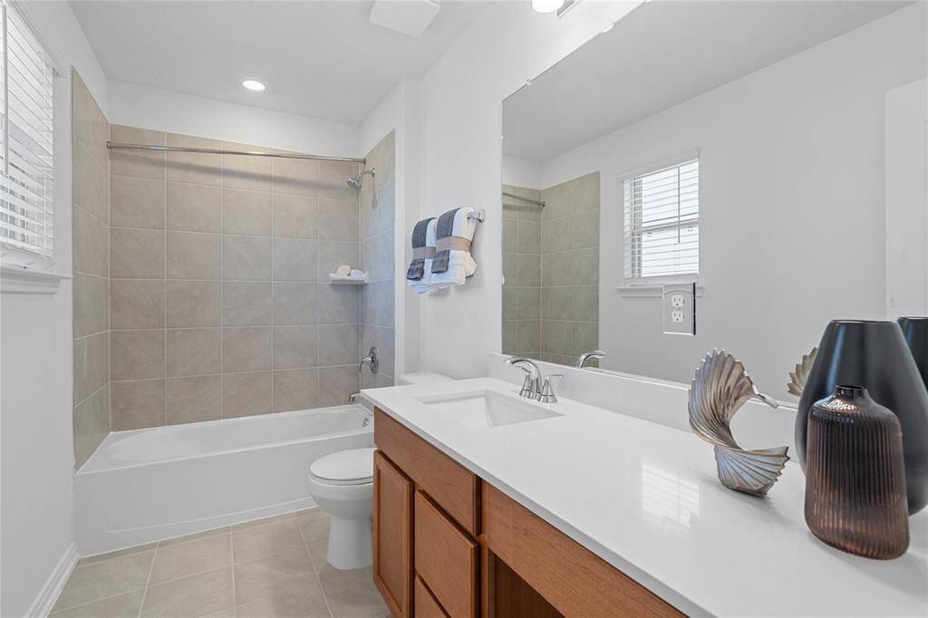 Secondary bath features tile flooring, bath/shower combo with tile surround, stained wood cabinets, beautiful light countertops, mirror, sleek fixtures and modern finishes.