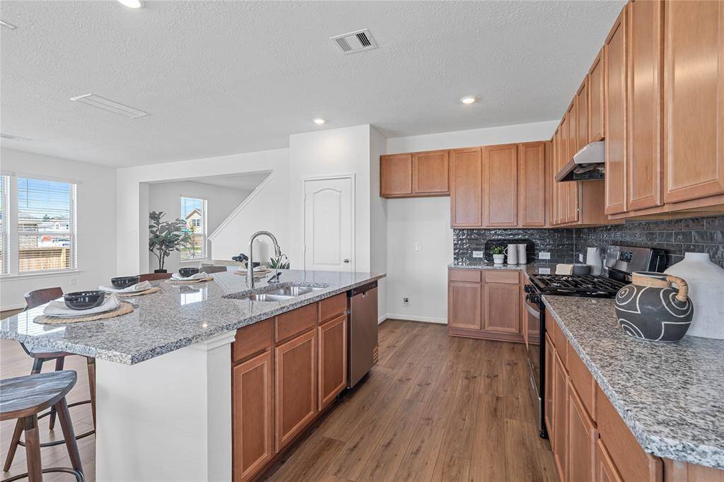 Another view of this spacious kitchen featuring high ceilings, stained wood cabinets, granite countertops, SS appliances, modern tile backsplash, recessed lighting, large kitchen island with space for a breakfast bar, and a pantry all overlooking your huge family room.