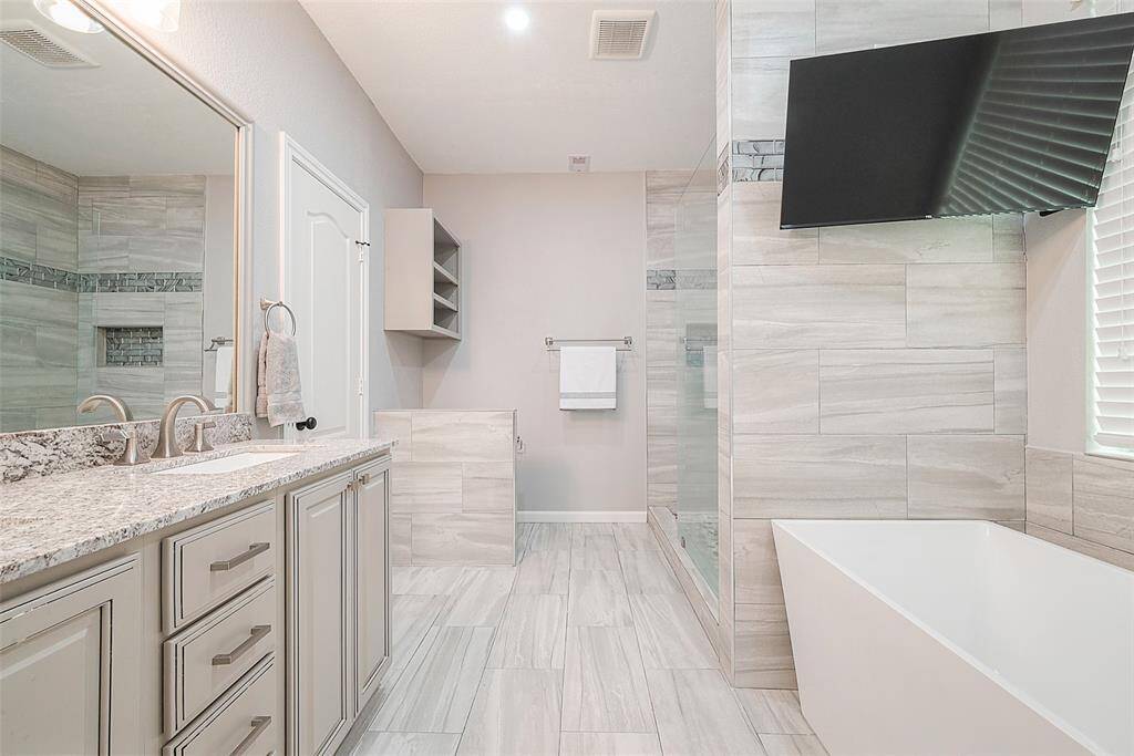 This modern bathroom features a spacious layout with a sleek freestanding bathtub, a large walk-in shower with glass doors, and a double vanity with granite countertops. The light-colored tiles and neutral tones create a bright and inviting atmosphere.