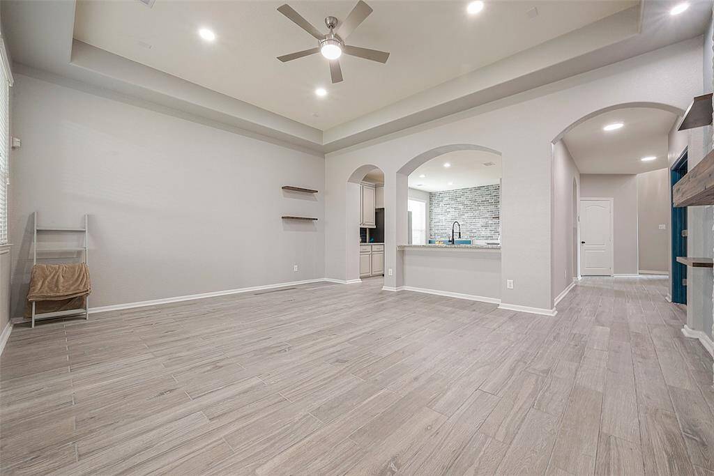 This photo showcases a spacious, modern open-concept living area with light wood flooring and a ceiling fan. It features a kitchen with a large archway, tiled backsplash, and ample counter space, creating a bright and inviting atmosphere.
