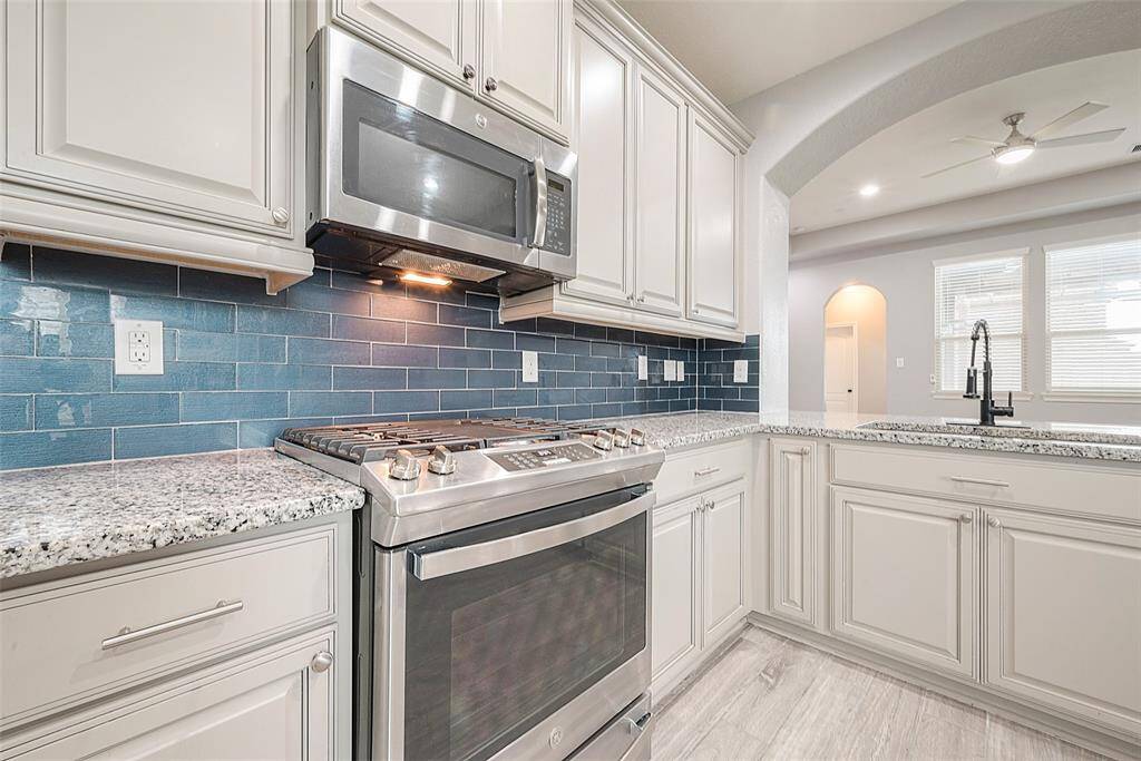 Modern kitchen featuring stainless steel appliances, sleek gray cabinetry, and a stylish blue subway tile backsplash. The space is bright and airy with ample counter space and an open layout leading into the living area. Perfect for cooking and entertaining.
