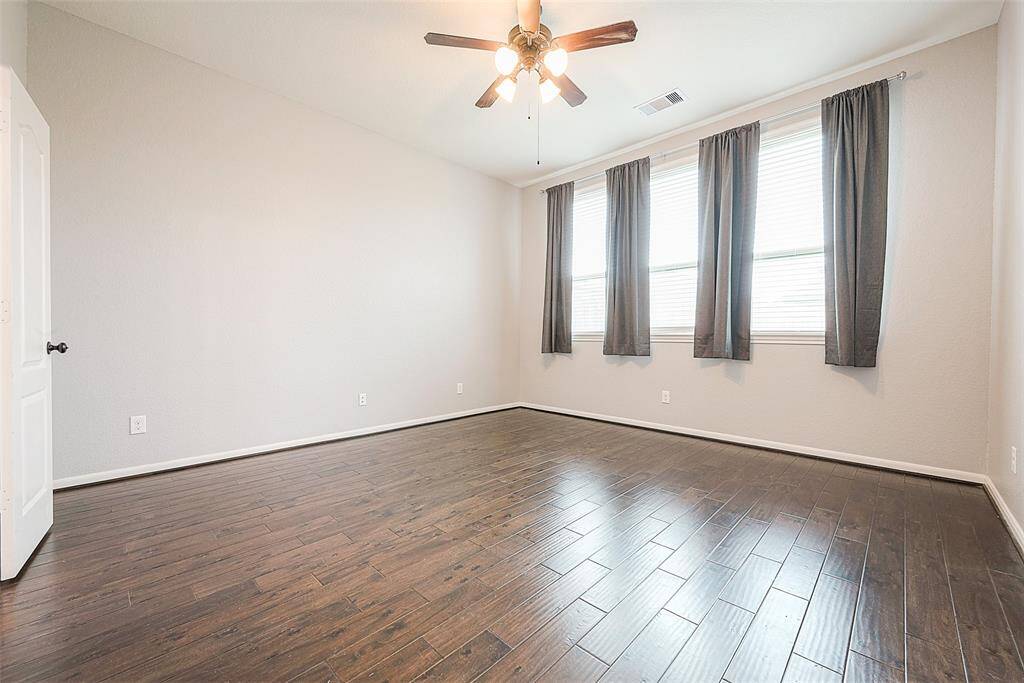 Spacious primary bedroom featuring elegant hardwood floors, ample natural light, and a ceiling fan for comfort.