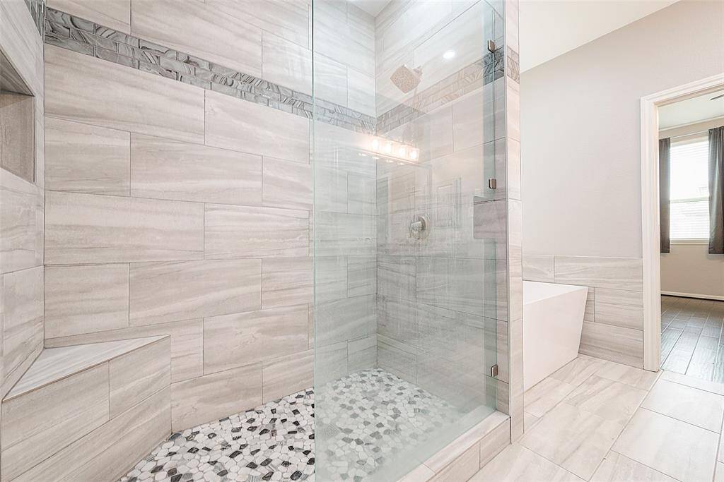 This photo features a modern bathroom with a spacious glass-enclosed shower, featuring elegant gray tile walls and a stone-patterned floor. Adjacent is a freestanding bathtub, all set in a bright, well-lit environment.