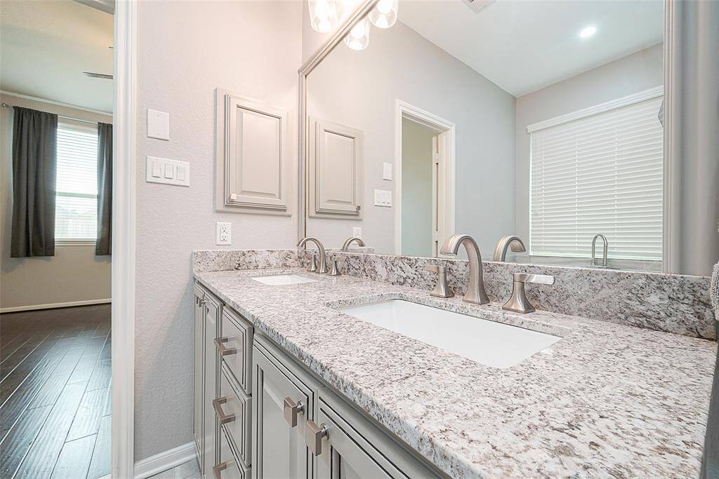 This photo showcases a modern bathroom with dual sinks, granite countertops, and sleek fixtures. The room features neutral tones and ample lighting, offering a bright and elegant space.