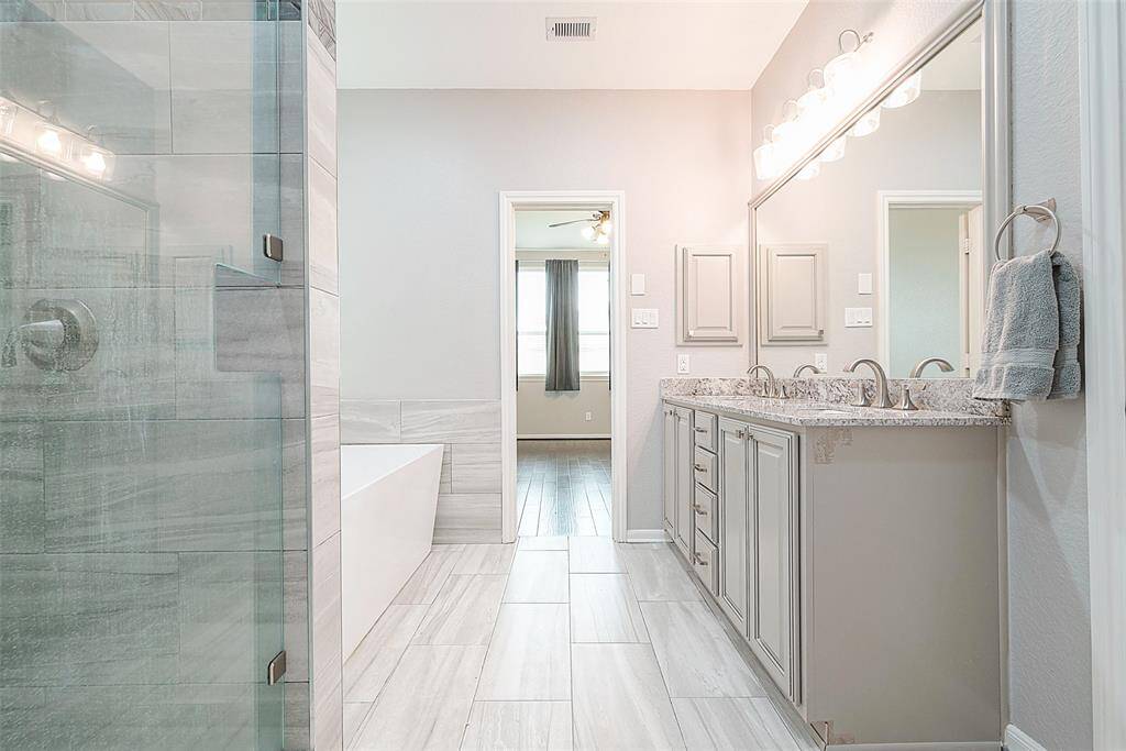 This photo showcases a modern bathroom featuring a spacious glass shower, a freestanding bathtub, dual sinks with granite countertops, and ample cabinet storage. The room is well-lit and has a neutral color palette, providing a clean and elegant atmosphere.