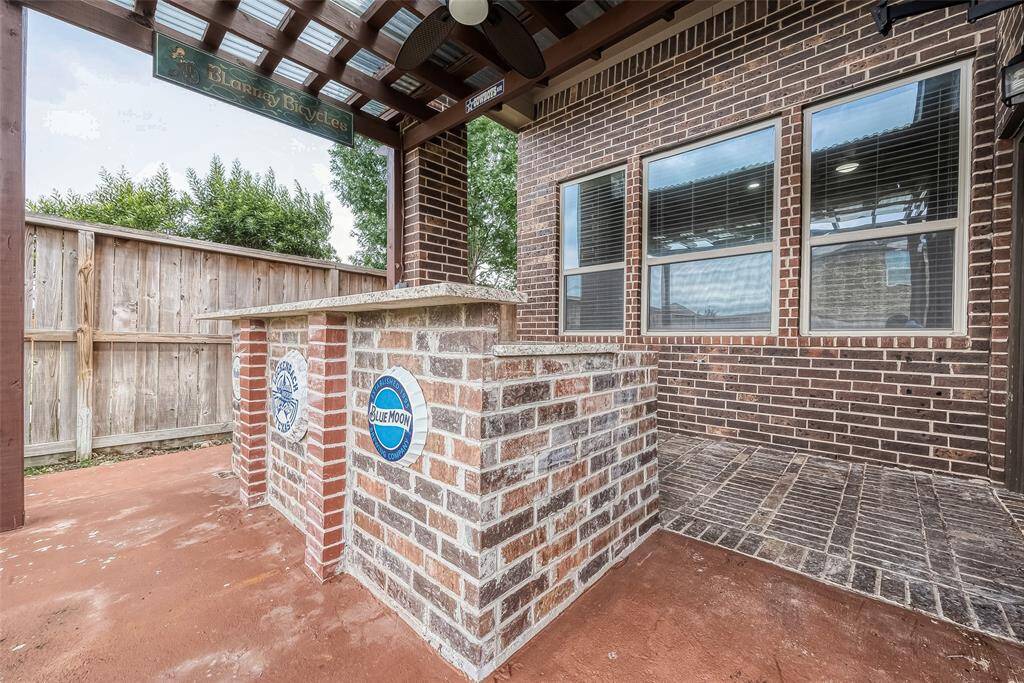 This outdoor space features a charming brick bar with decorative signage, set under a pergola. It offers a cozy entertaining area adjacent to the house, with a wooden fence providing privacy.
