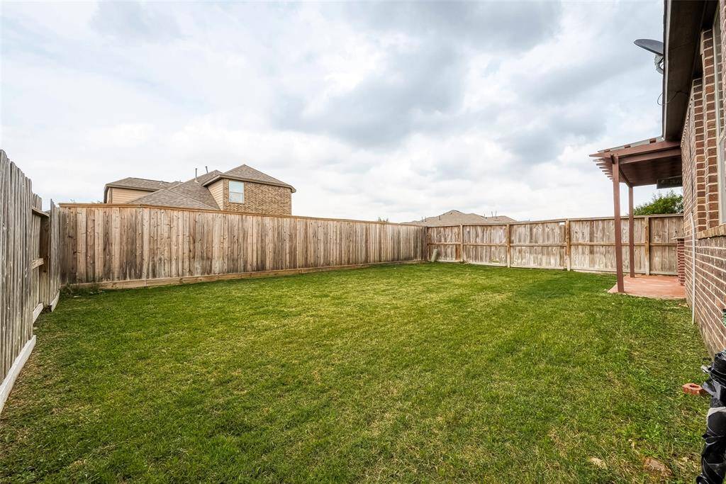 The photo shows a spacious backyard with a well-maintained lawn, enclosed by a wooden fence. Adjacent to the house, there is a small covered patio area. Perfect for outdoor activities and privacy.