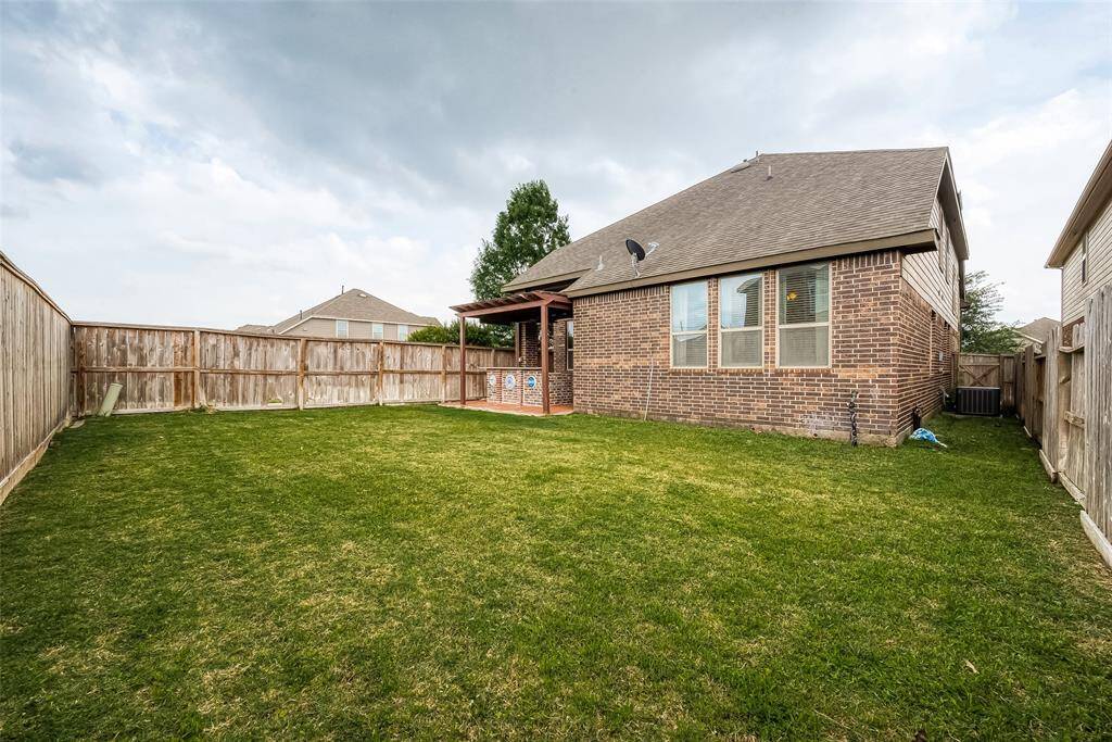 Spacious backyard with a well-maintained lawn, surrounded by a wooden privacy fence. The brick house features a covered patio area, providing a cozy outdoor space. Perfect for relaxation and entertaining.