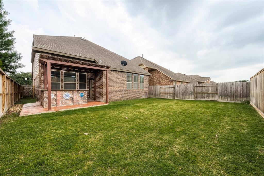 This photo shows a spacious backyard with a well-maintained lawn, enclosed by wooden fencing. The brick house features a covered patio area, perfect for outdoor relaxation or entertaining.
