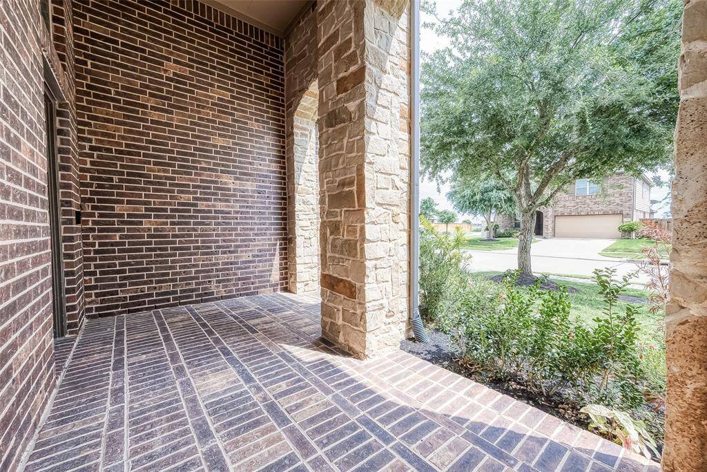 This photo shows a charming brick and stone entryway with a covered porch area. It opens to a view of a landscaped front yard and a quiet neighborhood street, perfect for welcoming guests.