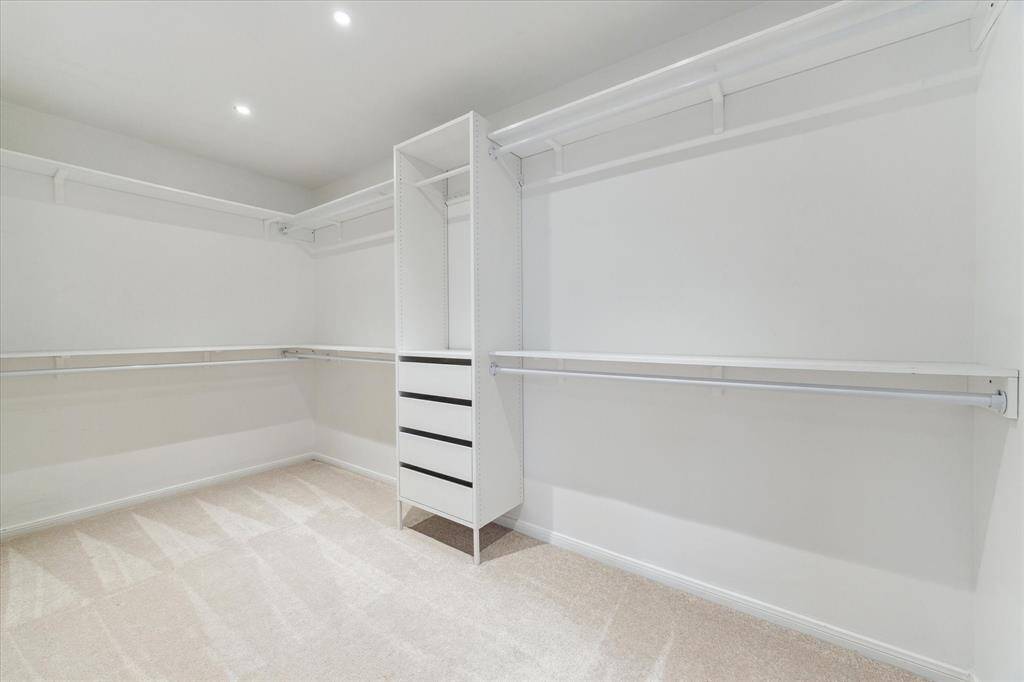 Primary closet with recent carpet (2024)built in shelves and drawers and recessed lighting